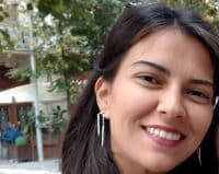 Kahverengi saçlı genç bir kadın dışarıda duruyor ve kameraya genişçe gülümsüyor. Gözleri neşeli bir ifadeyle kapalı ve dudakları hoş bir sırıtışla kıvrılmış. Üzerinde beyaz bir gömlek ve mavi bir kot pantolon var ve kollarını iki yana açmış. Arka planda beyaz bulutlarla bezeli mavi bir gökyüzü var. Rahat ve mutlu görünüyor, memnuniyetin mükemmel bir görüntüsü.