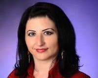 Bu, uzun siyah saçlı genç bir kadının görüntüsüdür. Üzerinde hafif bol parlak kırmızı bir gömlek var. Gözleri kapalı ve dudakları hafifçe ayrık, sanki rahatlamak için bir an ayırıyormuş gibi. Başı hafifçe eğik ve kollarını göğsünün üzerinde kavuşturmuş. Kendinden emin ve rahat bir duruşu var. Saçları omuzlarına dökülen yumuşak, doğal dalgalarla şekillendirilmiş. Yirmili yaşlarında olduğu anlaşılıyor ve yüzünde sıcak ve davetkâr bir ifade var. Bu anda dingin ve mutlu görünüyor.