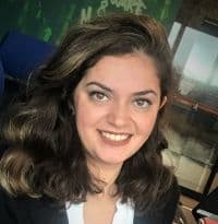 Genç bir kadın beyaz dişlerini göstererek kameraya doğru gülümsüyor. Parlak kahverengi gözleri ve yüzünden geriye doğru toplanmış uzun, siyah saçları var. Beyaz yakalı ve manşetli mavi bir gömlek ve beyaz bir etek giyiyor. Kollarını göğsünün önünde kavuşturmuş ve kendinden emin bir duruşu var. Yüzü yandan gelen ışıkla aydınlanmakta, sıcak ve davetkâr bir atmosfer yaratmaktadır. Rahatlamış ve mutlu bir halde görünüyor.