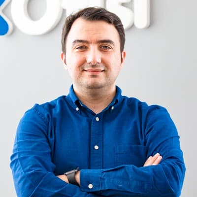 Bu resimde otuzlu yaşlarının ortasında, elektrik mavisi gömlek giymiş bir adam görülüyor. Kollarını kavuşturmuş ve yüzünde hafif bir gülümsemeyle içeride duruyor. Saçları koyu kahverengi ve kısa kesilmiş, güçlü bir çene hattı ve çenesi var. Fotoğrafın arka planının beyaz olması gömleğin parlak mavi renginin daha da öne çıkmasını sağlıyor.  Adamın giysisi uzun kollu, yakadan düğmeli ve göğüs hizasında iki cebi olan yakalı bir gömlekten oluşuyor. Kumaşın hafif pamuk ya da keten karışımı bir malzeme olduğu görülüyor, bu da gömleğe havadar bir his verirken havadaki herhangi bir soğuğa karşı da koruma sağlıyor. Kollar, daha fazla rahatlık ve stil puanı için dirseklerinin biraz üzerinde kıvrılmıştır!  Bir ayağı diğerinin biraz önünde olacak şekilde kendinden emin bir şekilde durur, bu da ona aşırı agresif veya korkutucu olmadan güven ve güç yayan otoriter bir duruş verir. Yüz ifadesi memnuniyeti yansıtıyor; rahat ama tetikte görünüyor - bir sonraki adımda ne olursa olsun üstesinden gelmeye hazır!