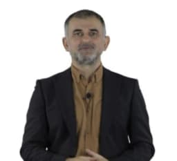 Takım elbiseli adam düz, beyaz bir arka planın önünde durmaktadır. Siyah, iki parçalı bir takım elbise ve açık mavi, uzun kollu bir gömlek giymektedir. Elleri önünde kenetlenmiş ve kendinden emin bir ifadeyle dümdüz karşıya bakıyor. Siyah saçları kısa kesilmiş ve düzgünce taranmış. Rahat ama profesyonel bir duruş sergiliyor. Sol kolunda bir saat ve siyah deri bir kemer takıyor. Görünüşü sofistike ve dengeli.