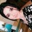 Bu fotoğrafta açık mavi bir tişört ve bir çift kot şort giyen genç bir kadın selfie çekerken görülüyor. Koyu kahverengi saçları dağınık bir şekilde toplanmış ve yüzünde parlak bir gülümseme var. Doğrudan kameraya bakıyor, gözleri geniş ve başı hafifçe eğik. Kollarını uzatmış, sol eliyle anı yakalamak için önünde bir cep telefonu tutuyor. Arka plan düz beyaz bir duvar ve görünürde hiçbir süsleme yok. Kadının duruşu rahat ve eğlenceli, memnuniyet ve neşe hissi veriyor. Hayatının bu enstantanesinde, bir mutluluk anını yakalamayı ve bunu dünyayla paylaşmayı seçmiştir.