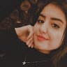 Genç bir kadın beyaz bir duvarın önünde durmuş, akıllı telefonuyla selfie çekiyor. Üzerinde pembe çiçek desenli sarı bir elbise var ve koyu renk saçları yüksek bir at kuyruğu şeklinde geriye doğru toplanmış. Bir kolunu uzatmış ve diğer kolunu dirseğinden bükmüş halde telefonu önünde tutmaktadır. Selfie çekerken gözleri kapalı ve ışıl ışıl gülümsüyor. Diğer elini kalçasına dayamış, kendinden emin ve mutlu ifadesini vurguluyor.