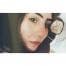 Bu görüntüde akıllı telefon kamerasıyla selfie çeken genç bir kadın görülüyor. Açık mavi bir tişört giyiyor, saçlarını topuz yapmış ve yüzünde ciddi bir ifade var. Beyaz duvarları ve sağda bir penceresi olan bir odada duruyor. Sağ elinde telefonu yüzünün önünde tutuyor ve sol eli görüntünün köşesinde görülebiliyor. Kendinden emin ama ciddi bir duruşu var ve pencereden gelen ışık yüzünü aydınlatıyor. Hatırlamak istediği bir anı yakalamaya hazır görünüyor.