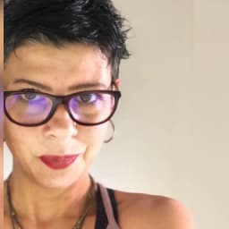 Genç kadın yüzünde bir gülümsemeyle selfie çekiyor. Üzerinde beyaz bir tişört ve mavi bir kot pantolon var. Saçları at kuyruğu şeklinde bağlanmış ve telefonunu iki eliyle tutuyor. Gri bir duvarın önünde duruyor ve arkasındaki büyük pencereden içeri güneş giriyor. Gözleri parlak ve anlamlı, yüz ifadesi ise neşe ve memnuniyet dolu. Belli ki anın tadını çıkarıyor ve vücudu dik, kendinden emin bir duruşta. Modern, kendine güvenen bir kadının mükemmel bir resmi.
