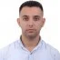 Kameranın önünde düz beyaz bir gömlek giymiş bir adam durmaktadır. Gülümsüyor, elleri cebinde ve doğrudan kameraya bakıyor. Saçları kısa ve yana doğru taranmış, çenesinde az miktarda kirli sakal var. Aydınlık ve güneşli bir ortamda dururken memnun ve rahat görünüyor. Beyaz gömleği canlı mavi gökyüzüne ve yemyeşil ağaçlara karşı göze çarpıyor. Kendinden emin ve arkadaş canlısı görünüyor ve herhangi bir görüntü başlığı veri kümesine harika bir katkı sağlayacağı kesin.
