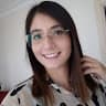 Bu, dişlerini göstererek gülümseyen gözlüklü genç bir kadının görüntüsüdür. Omuzlarına dökülen koyu renk saçları var ve ince metal çerçeveli gözlükler takıyor. Gözleri parlak ve yanakları pembe. Mavi bir gömlek giyiyor ve yüzünde memnuniyetini ve mutluluğunu gösteren sıcak bir gülümseme var. Burnu hafifçe kalkıktır ve dudakları gülümseme şeklinde kıvrılmıştır. Çenesi hafifçe sivri ve başı hafifçe yana eğik, bu da ona yaramaz bir görünüm veriyor. Harika vakit geçiriyor gibi görünüyor ve çok iyi bir ruh hali içinde.