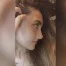Bu bir kadının yüzünün yakın çekim fotoğrafı. Sıcak, pembe bir alt tona sahip açık tenli görünüyor. Gözleri badem şeklinde ve kaşları ince ve zarif bir şekilde kemerli. Dudakları dolgun ve dolgun ve burnu küçük, düğme benzeri bir şekle sahip. Sağ yanağında, burnunun yanında bir güzellik izi vardır. İfadesi nazik ve huzurlu, bir parça da memnuniyet içeriyor. Çenesinde küçük bir gamzesi vardır ve saçları yüzünden geriye doğru taranmıştır. Öne çıkan ve parlayan çok doğal, klasik bir güzelliği var.
