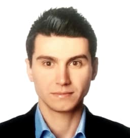 Resimdeki adam gri bir takım elbise giyiyor ve altında beyaz bir gömlek var. Düzgün, kısa siyah saçları ve temiz traşlı bir yüzü var. Parke zeminli, beyaz duvarlı ve arkasında pencere olan bir odada duruyor. Kendinden emin görünüyor, bakışları doğrudan ve duruşu dik. Elleri önünde kenetlenmiş ve sol bileğinde bir saat takılı. Kırklı yaşlarının ortasında ve profesyonelce giyinmiş görünüyor. İyi giyimli bir iş adamının mükemmel bir örneği.