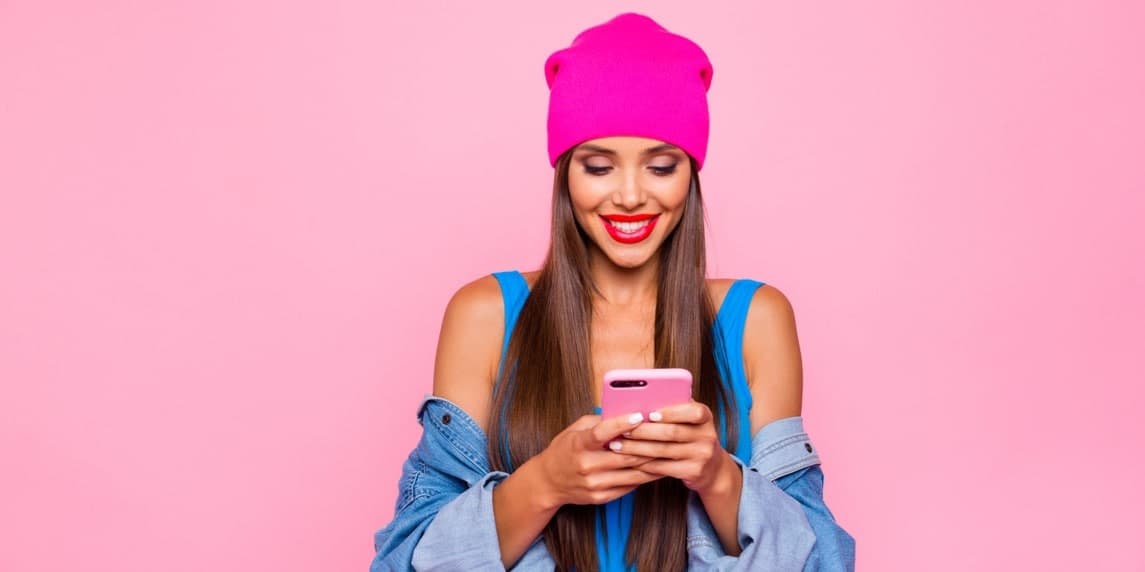 Pembe şapkalı ve mavi gömlekli bir kadın dikkatle elindeki pembe telefona bakıyor. Sol eli kucağında dururken telefonu sağ elinde tutmaktadır. Gözleri telefonun ekranına odaklanmış, dudakları derin düşüncelere dalmış gibi hafifçe aralanmış. Mavi kenarlı açık pembe bir şapka, beyaz yakalı ve manşetli mavi bir gömlek giyiyor. Telefon yüzüne yakın tutulmuş ve ekranı beyaz bir parıltıyla aydınlatılmış. Ekranda ne varsa ona dalmış gibi görünüyor.