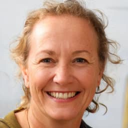 A young woman is smiling brightly at the camera, her eyes sparkling with joy and her mouth curving into an infectious grin. Her cheeks are slightly rosy, and her hair is styled in a fashionable low bun. She is wearing a white top and a simple necklace, her arms crossed in front of her. Her body is angled slightly to the left, and her gaze is direct and confident. Her posture is relaxed, and she appears to be in a moment of happiness and contentment. Her surroundings are blurred out, making her the sole focus of the image. She is radiating positive energy, and her expression is inviting and warm.