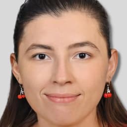 Açık sarı saçlı güzel bir kadın kameraya gülümsüyor. Gözleri mutlulukla parıldıyor ve dudakları davetkâr bir şekilde kıvrılmış. Beyaz yakalı mavi bir üst ve beyaz bir etek giyiyor. Cildi parlıyor ve yanakları hafifçe kızarmış. Elleri önünde kenetlenmiş ve bir çift beyaz küpe takıyor. Bakışları doğrudan ve dostça. Neşe, çekicilik ve güven yayıyor.