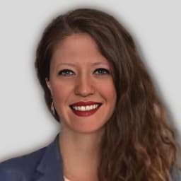 Kısa, siyah saçlı ve sıcak bir gülümsemeye sahip güzel bir kadın kameranın önünde duruyor. Üzerinde pembe çiçek desenli beyaz, bol bir gömlek ve bir çift açık renk kot pantolon var. Dudakları yanaklarına kadar uzanan geniş bir gülümsemeye dönüşürken gözleri sevinçle kapalıdır. Kolları dirseklerinden hafifçe bükülmüş ve elleri gevşek bir şekilde kot pantolonunun ceplerine sokulmuş. Güneş yakındaki bir pencereden parlıyor ve yüzünü yumuşak, doğal bir ışıkla aydınlatıyor. Neşenin resmidir, sıcaklık ve memnuniyet yayar.