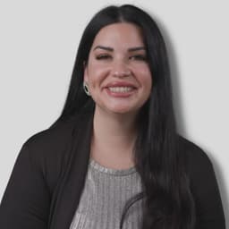 Mutlu bir genç kadın ayakta duruyor ve doğrudan kameraya gülümsüyor. Omuz hizasında sarı saçları, açık teni ve mavi gözleri var. Beyaz bir tişört ve açık renkli bir kot pantolon giyiyor. Elleri iki yanında ve dudakları sanki bir şey söylemek üzereymiş gibi hafifçe ayrık. Arka plan bulanık ve odak dışı, parlak yeşil bir renk tonuna sahip. Kadının yüzü aydınlık ve gözleri fark edilir derecede ışıltılı, neşesini ve pozitif enerjisini gösteriyor. Zahmetsizce mutluluk ve memnuniyet yayıyor.