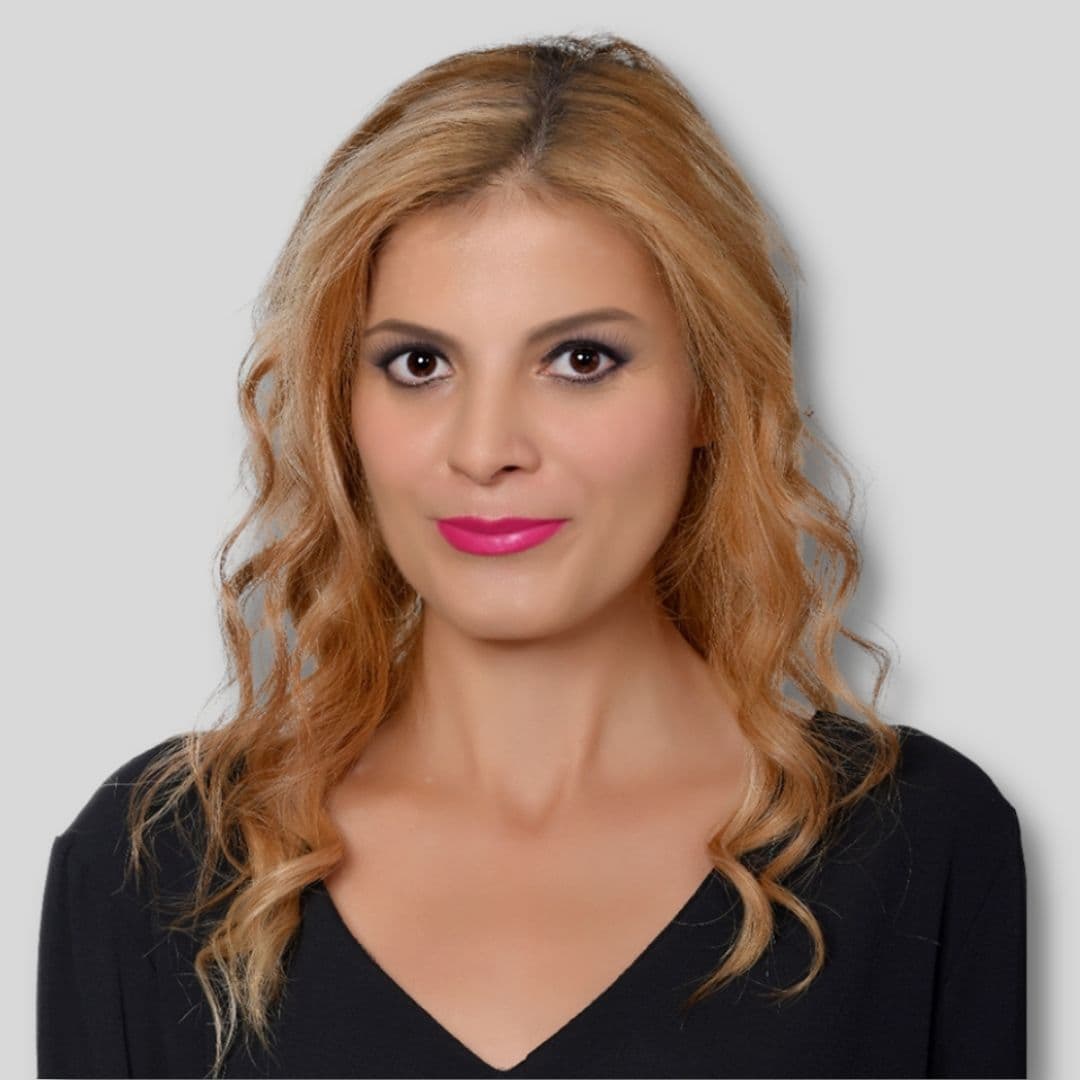 A woman with long blonde hair is standing in front of the camera wearing a black top. She has her arms crossed and a serious expression on her face. The dark color of the top contrasts with her pale skin, creating a striking image. Her hair is styled in a sleek look that is shining in the light. Her eyes are focused on something in the distance. Her posture suggests a determined and confident attitude. She looks like she is ready to take on any challenge that comes her way.