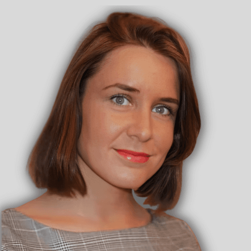 This is a closeup photograph of a young woman with short, brown hair. She has a pleasant expression on her face. Her eyes are deep brown and have an intelligent glint. Her nose is small and slightly upturned. Her lips are full and have a subtle pink hue. Her cheeks are lightly dusted with a natural blush. Her jawline is well-defined and her hair is cut in a neat bob that sits just above her shoulders. Her hair has lovely natural waves to it and frames her face nicely. She looks confident, comfortable, and natural in her own skin.