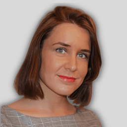 This is a closeup photograph of a young woman with short, brown hair. She has a pleasant expression on her face. Her eyes are deep brown and have an intelligent glint. Her nose is small and slightly upturned. Her lips are full and have a subtle pink hue. Her cheeks are lightly dusted with a natural blush. Her jawline is well-defined and her hair is cut in a neat bob that sits just above her shoulders. Her hair has lovely natural waves to it and frames her face nicely. She looks confident, comfortable, and natural in her own skin.