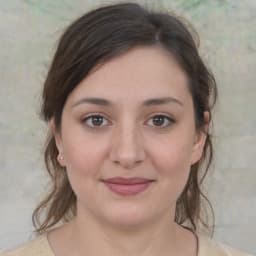 Bu, uzun, dalgalı, kahverengi saçlı ve ten rengi gömlekli bir kadının resmi. Açık tenli ve parlak bir gülümsemesi var. Gözleri kahverengi ve burnu sivri. Dudakları hafifçe ayrılmış ve çenesi hafifçe kalkık. Çenesinde küçük bir güzellik izi var ve yanakları hafifçe kızarmış. Bir kolye takıyor ve saçları at kuyruğu şeklinde geriye doğru toplanmış. Rahat ve memnun görünüyor. Duruşu kendinden emin ve bakışları ileriye dönük. Arkadaş canlısı ve davetkar görünüyor.