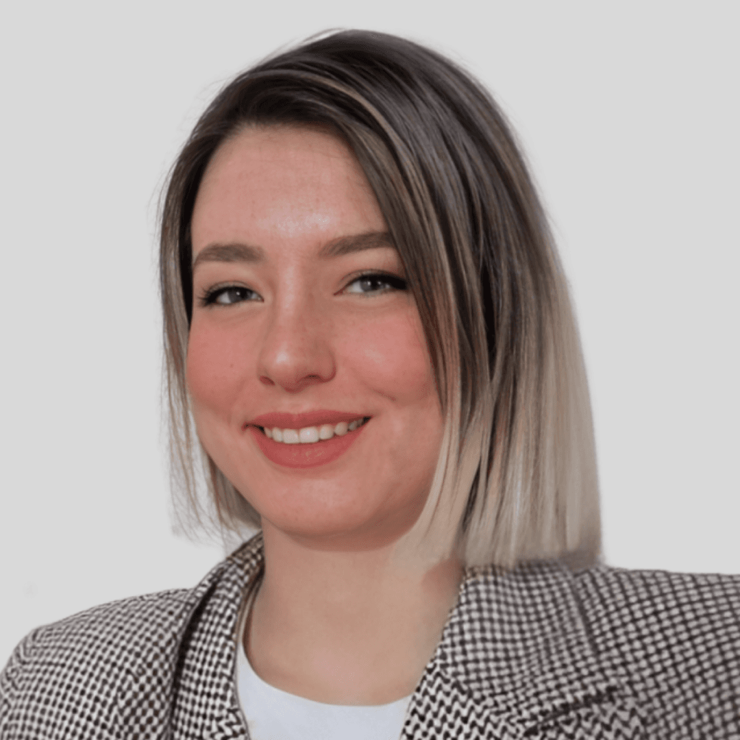 Yüzünde parlak bir gülümseme olan genç bir kadın doğrudan kameraya bakıyor. Uzun siyah saçları, koyu kahverengi gözleri ve açık bir teni var. Mavi-gri bir kazak, beyaz kot pantolon ve siyah botlar giyiyor. Dudakları hafifçe ayrılmış ve gözleri neşe ve mutluluk dolu. Başı hafifçe yana eğik, bu da gülümsemesinin daha da sıcak görünmesini sağlıyor. Bu anda kendinden emin ve memnun görünüyor, parlak gözleri ve gülümsemesi neşe saçıyor.