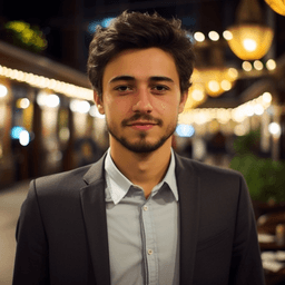 Bu görüntü yirmili yaşlarının ortasında resmi bir takım elbise giyen genç bir adamı tasvir ediyor. Dışarıda bir sokakta ayakta durmaktadır ve fotoğrafın arka planı siyahtır. Adamın kısa koyu kahverengi saçları var ve yakalı, önden düğmeli bir elbise gömleği giyiyor. Yüzünde çenesini güzelce çerçeveleyen etkileyici bir bıyık ve sakal kombinasyonu var. Bir eli rahatça cebinde dururken diğer eliyle çerçevenin dışında bir şey tutarak dik dururken kendinden emin görünüyor. Kıyafeti pantolon, elbise ayakkabısı ve omuzlarındaki jartiyer ya da askı gibi görünen şeylerden oluşuyor ve bu da genel sofistike görünüme katkıda bulunuyor. Bu resim onu uzaklara bakarken ve gizemli bir hava içinde yakalıyor - belki de düşüncelere dalmış ya da sadece o anda onu çevreleyen her şeyi düşünüyor.